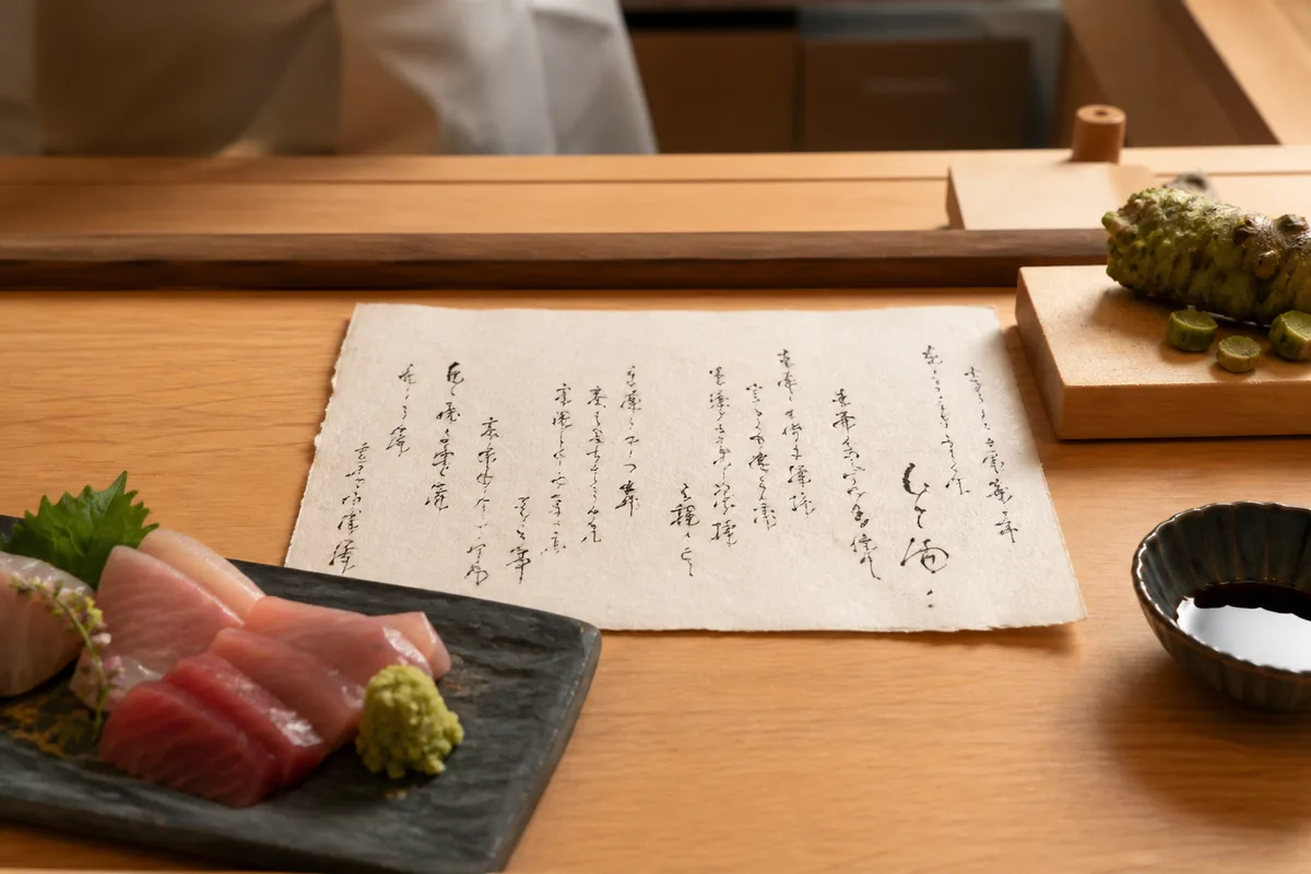 Carte manuscrite de restaurant japonais posée sur une table en bois clair